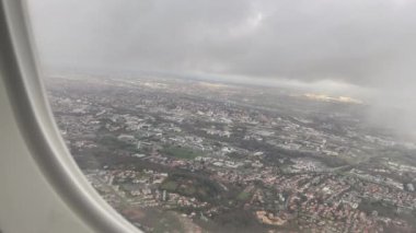  City view seen from up in the air airplane window with clouds. Closeup plane window passenger POV looking down from sky.