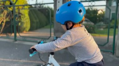 One little boy riding bicycle in city street sidewalk. Child wearing protective helmet rides bike outdoors