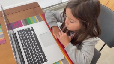 Dizüstü bilgisayarın önündeki kız çocuk. Küçük kız balkonda modern teknolojiyle eğlence medyasına bakıyor.