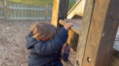 Child climbing playground structure outdoors. Happy kid playing outside during winter season wearing jacket. Lifestyle active kid 