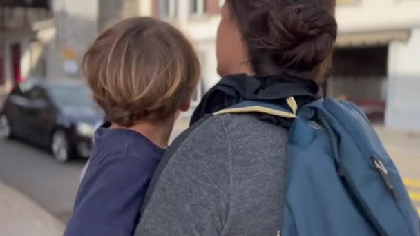 在阳光明媚的日子里 母亲背着孩子在欧洲大街上散步 父母抱着小男孩旅行观光 — 图库视频影像