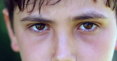 Serious angry child frowning to camera. Close-up of young boy staring macro eyes detail closeup