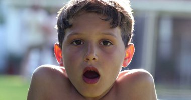 Male kid face portrait with eyes closed. Handsome child in sunlight outside opening eye