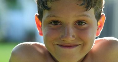 Handsome young boy child face smiling feeling happy and joy in outdoor sunlight. Kid portrait real life smile