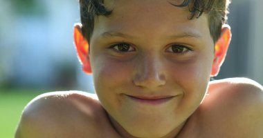 Handsome young boy child face smiling feeling happy and joy in outdoor sunlight. Kid portrait real life smile