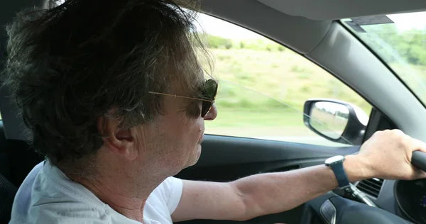Senior man driving on country road. Retired older man enjoying drive holding steering wheel