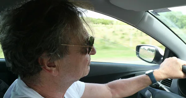 Senior man driving on country road. Retired older man enjoying drive holding steering wheel