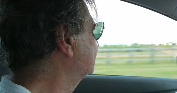 Profile of older man face driving on road with landscape passing by