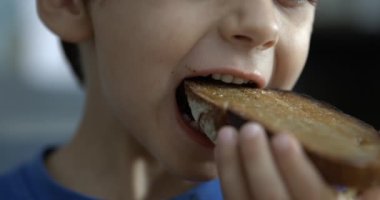 Küçük çocuk tost ekmeği yiyor, çocuk ağzı süper yavaş çekimde hız rampasında bir ısırık alıyor.