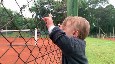 Baby infant holding into tennis fence watching game