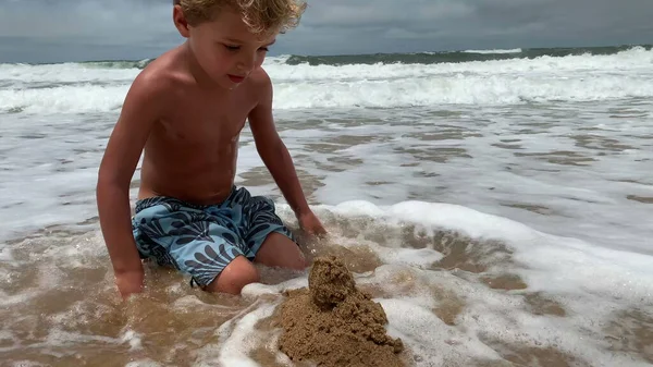 Child attempting to build sandcastle. Ocean wave coming to shore destroying kid effort to build castle, perseverance concept