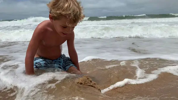 Child attempting to build sandcastle. Ocean wave coming to shore destroying kid effort to build castle, perseverance concept