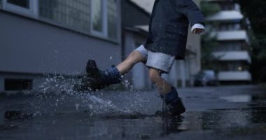 Sokağın ortasındaki su birikintisini tekmeleyen çocuğun yüksek hızlı kamerayla tek başına eğlendiği nostaljik bir sahne.