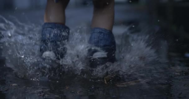 雨のブーツの子供のクローズアップ 高速捕獲とプードルに飛び散る 水たまりに飛び込むレインウェアの子供の足 — ストック動画