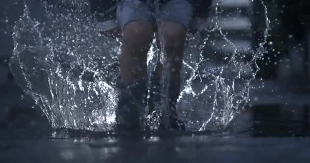エキサイティングな子供は 雨のブーツを着用して 高速カメラ 雨季と空気中の滴をキャプチャするスローモーションで水プードルにジャンプします — ストック動画