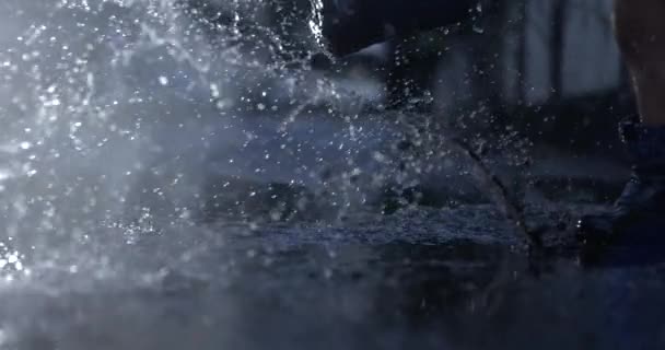雨のブーツを着ている子供は雨の後 通りの外で水プドルを蹴って水を飛ばします — ストック動画