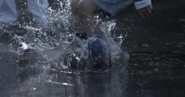高速で捕獲された雨の日に楽しむ雨のブーツを着た子供たちは どこにでもゆっくり動く水の水プドルに飛び込む遊び心のある子供の足 — ストック動画