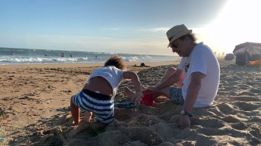 Büyükbabam ve küçük torunum kumsalda oynuyorlar.