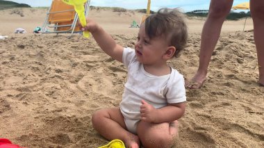 Yavru kumsalda kum ve kürekle oynuyor.