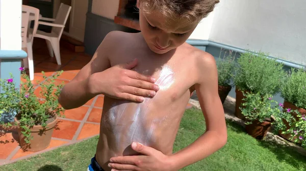 Child rubbing sunblock lotion into body chest. Young boy applying sunscreen protection