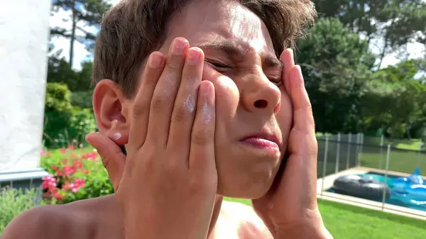 Child rubbing screen lotion to face. Sun tan prevention. Kid sunblock