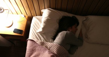 Sleepless woman turning bedside light on leaning on side suffering from insomnia