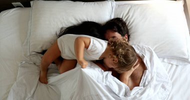 Cute family moment. Infant entering couple bed in the morning. Baby intruding in father and wife cuddle moment