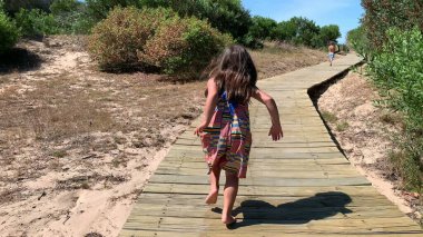 Little girl child running towards beach or wooden pathway