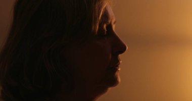 Anxious older woman suffering at night, close-up face. Troubled person rubbing face with hand