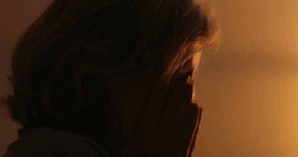 Anxious older woman suffering at night, close-up face. Troubled person rubbing face with hand