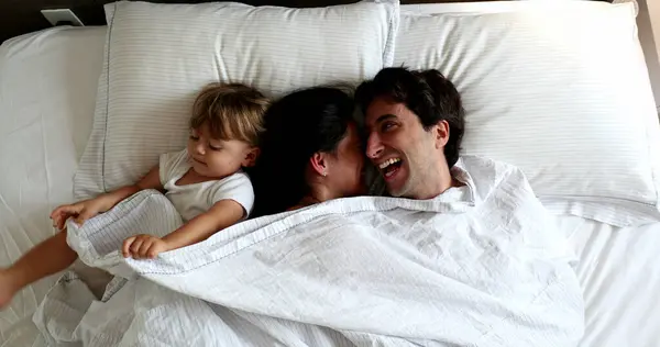 Cute family moment. Infant entering couple bed in the morning. Baby intruding in father and wife cuddle moment