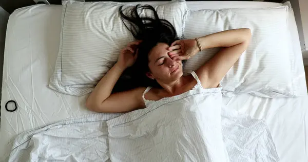 Woman waking up in the morning lying in bed, top view perspective
