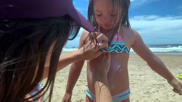 Mom applies sunscreen to little girl. Parent rubbing sunblock to daughter skin