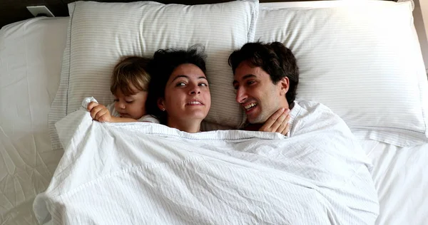 Cute family moment. Infant entering couple bed in the morning. Baby intruding in father and wife cuddle moment
