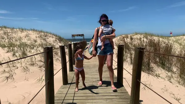 Mother walking away from beach with kids on wooden pathway