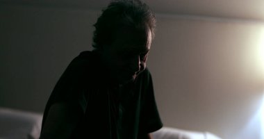 Worried senior man sitting by the side of the bed in the night unable to sleep due to stress and worry