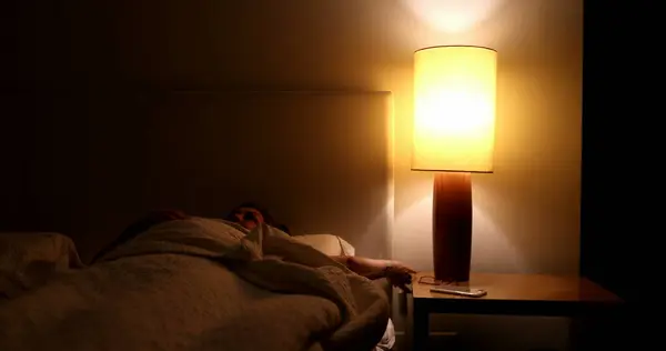 Woman prepares to go to bed and sleep. Person lays down in bed and turns off night stand besides bed