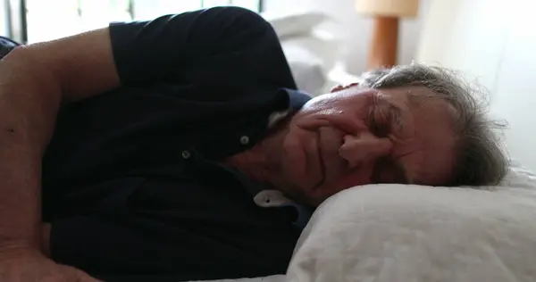 Senior man lays down in bed to sleep. Older person napping resting