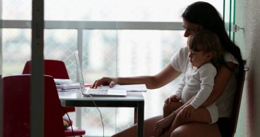 Candid toddler boy on mother lap watching video on computer laptop at home