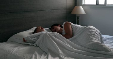 Mother and baby toddler in bed. cute family domestic life moment in the morning, infant hiding under blanket