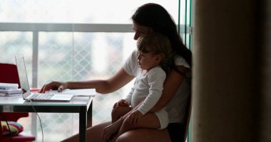 Candid toddler boy on mother lap watching video on computer laptop at home