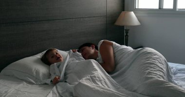 Mother and baby toddler in bed. cute family domestic life moment in the morning, infant hiding under blanket