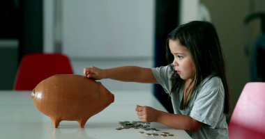 Little girl adding coins inside piggy bank. Child saving money concept