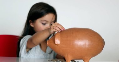 Little girl adding coins inside piggy bank. Child saving money concept