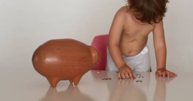 Child saving money adding coins inside piggy bank