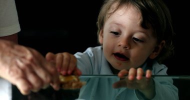 Cute toddler baby boy leaning on glass table with hands peeking, looks at camera
