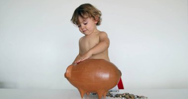 Adorable baby boy adding savings inside piggy bank