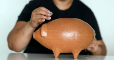 Person saving money putting pennies inside piggy bank