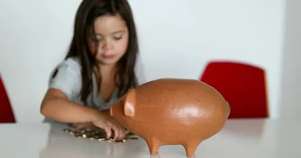 Little girl saving money inside piggy bank