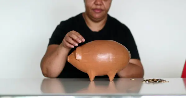 African woman inserting coins inside piggy bank